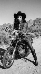 fashion model in pink dress and cowboy hat sitting on motorcycle in desert landscape